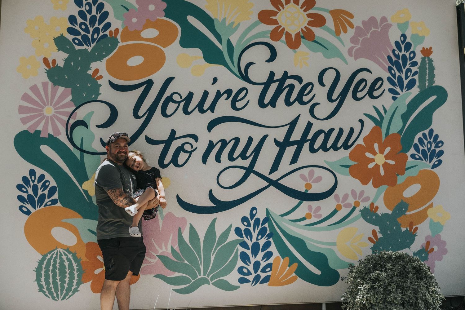 Colorful floral mural on white wall with decorative text and greenery elements in teal, orange and pink tones.