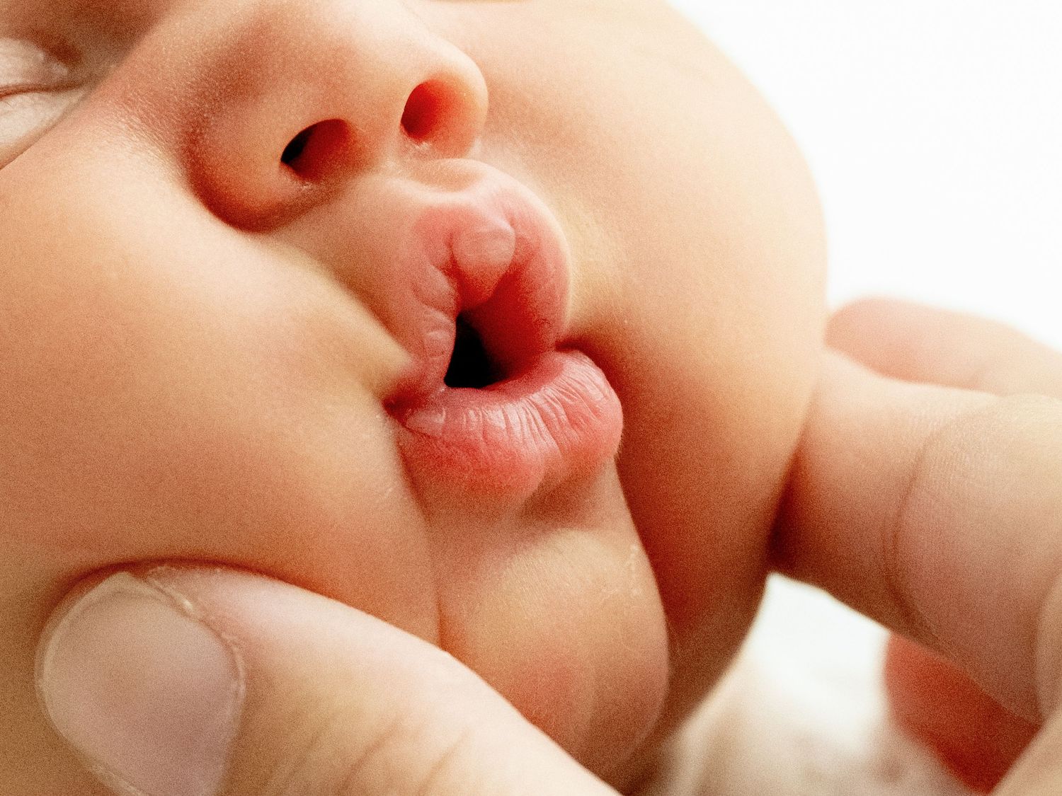 Close-up macro shot of a baby's tiny lips and nose with fingers reaching towards mouth.