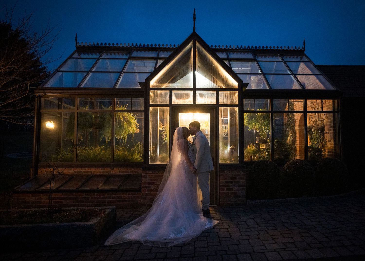 Newlyweds share an intimate moment outdoors with autumn foliage and rustic architecture in background.