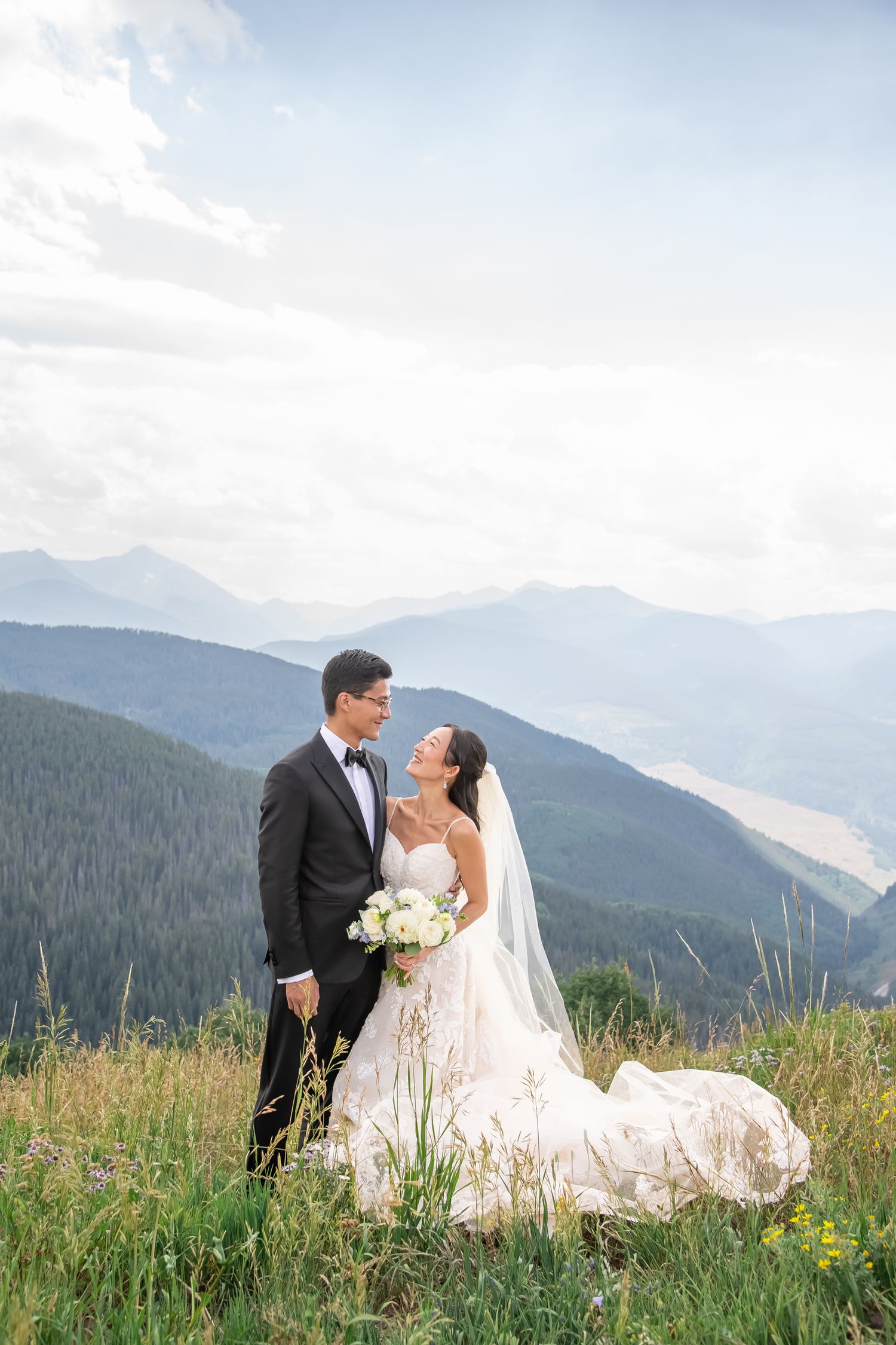 Wedding couple embracing in mountain meadow with dramatic mountain peaks in background.