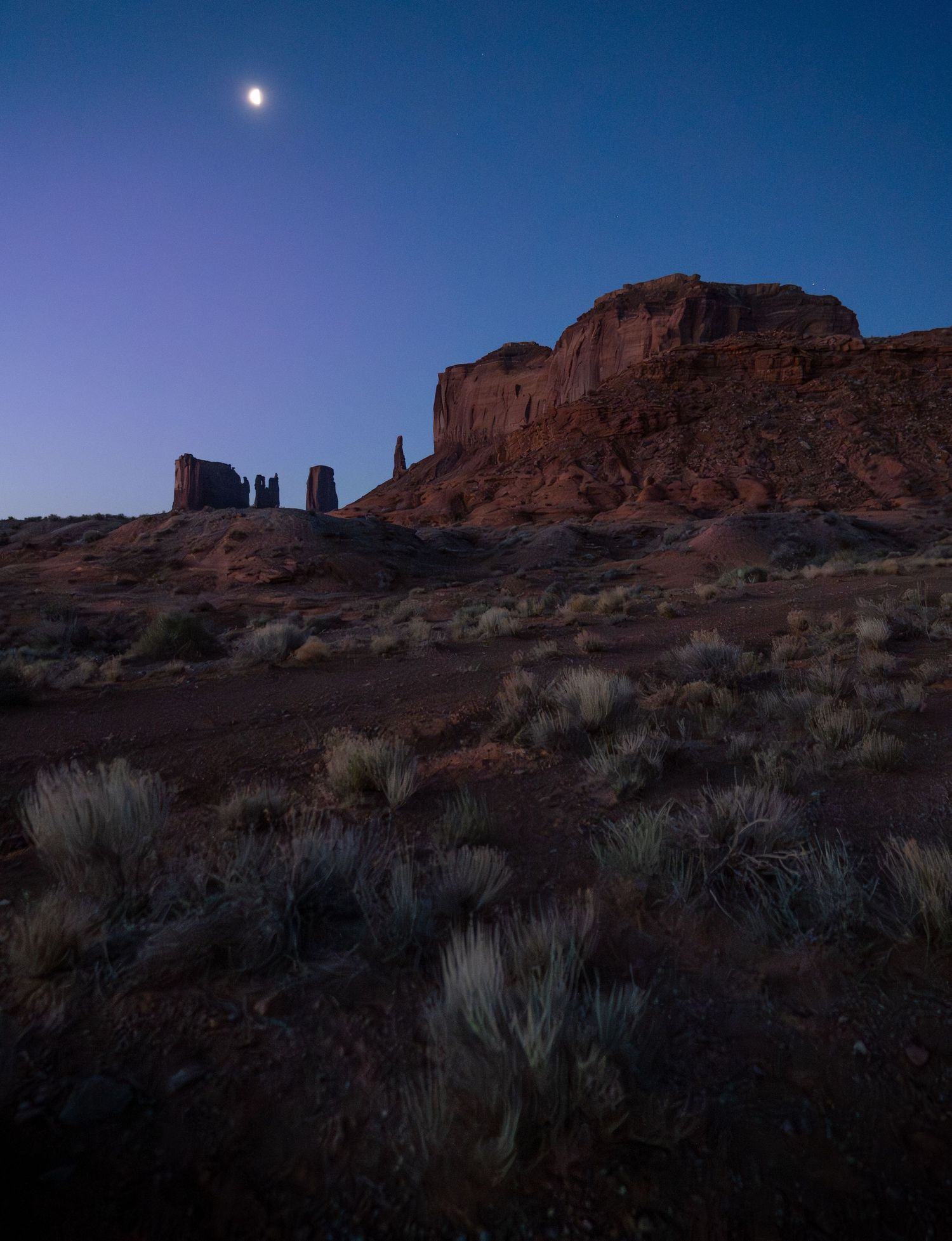 A series of silhouetted figures stand against a sunset sky viewed through natural rock arches in a desert landscape.