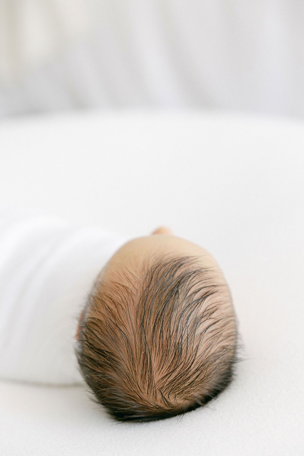Close-up view of a baby's head with soft brown hair resting on white bedding. CT photographer