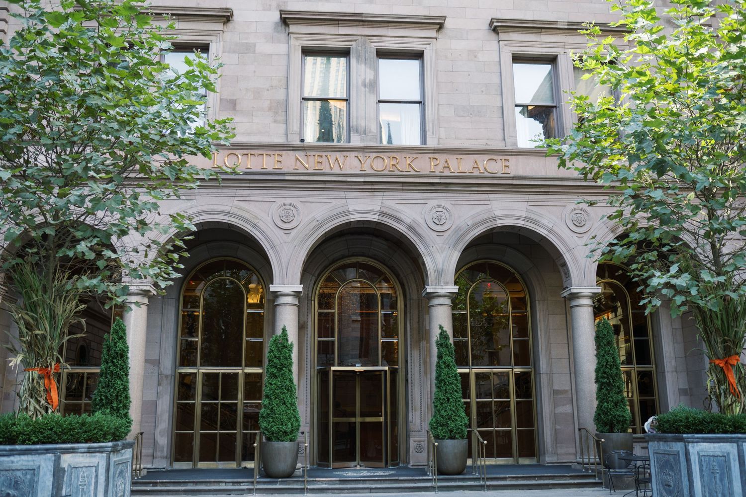 Historic stone building facade with arched windows and columns features ornate architectural details and lush greenery.