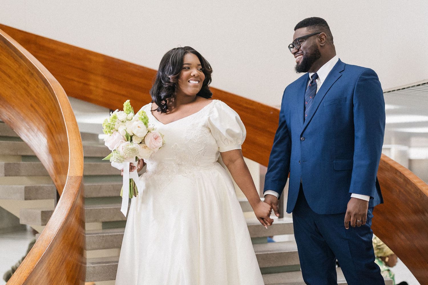 A couple in wedding attire shares a tender moment together on a staircase with white decor.