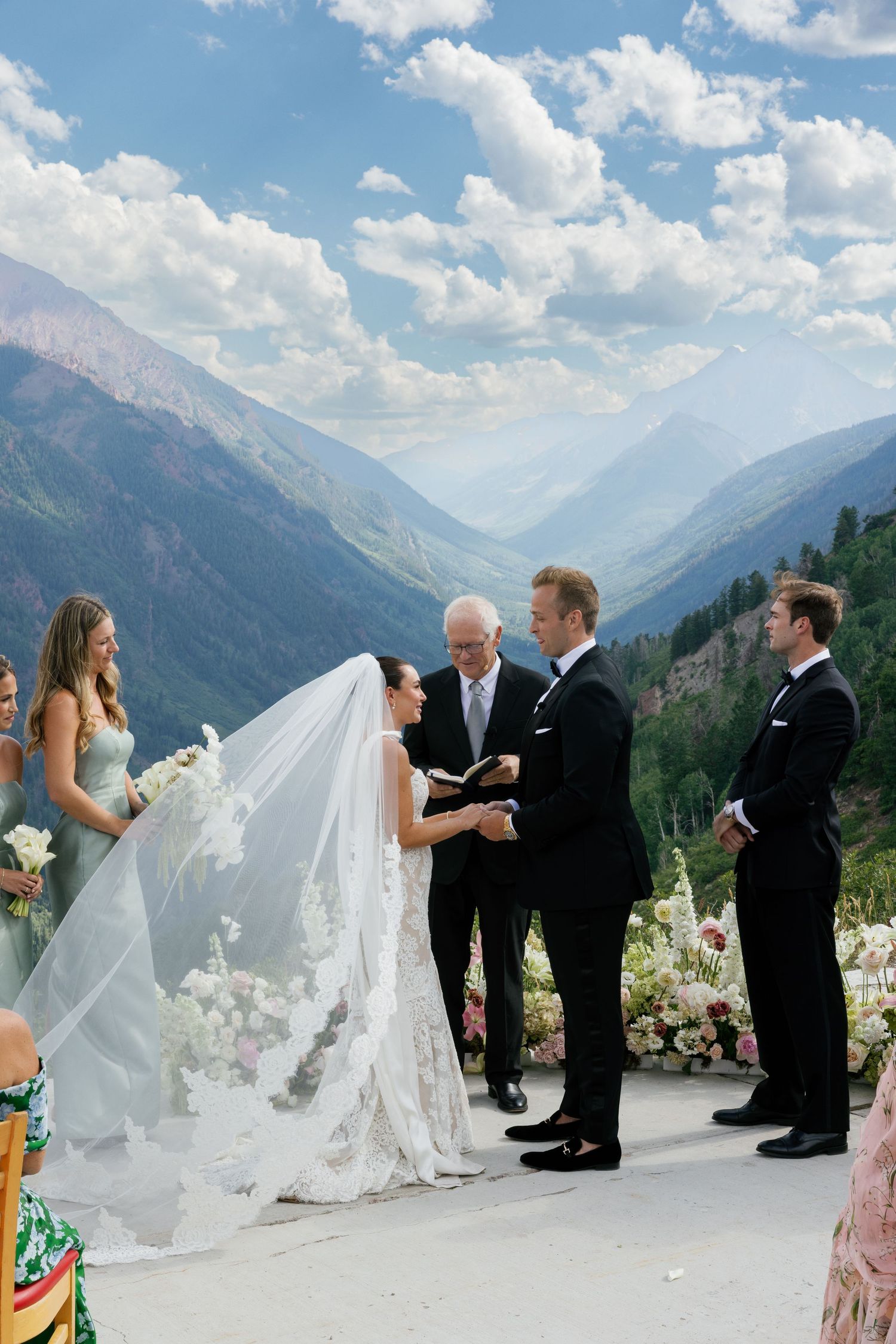 Wedding party walking along a mountain ridge against a dramatic blue sky with white clouds.
