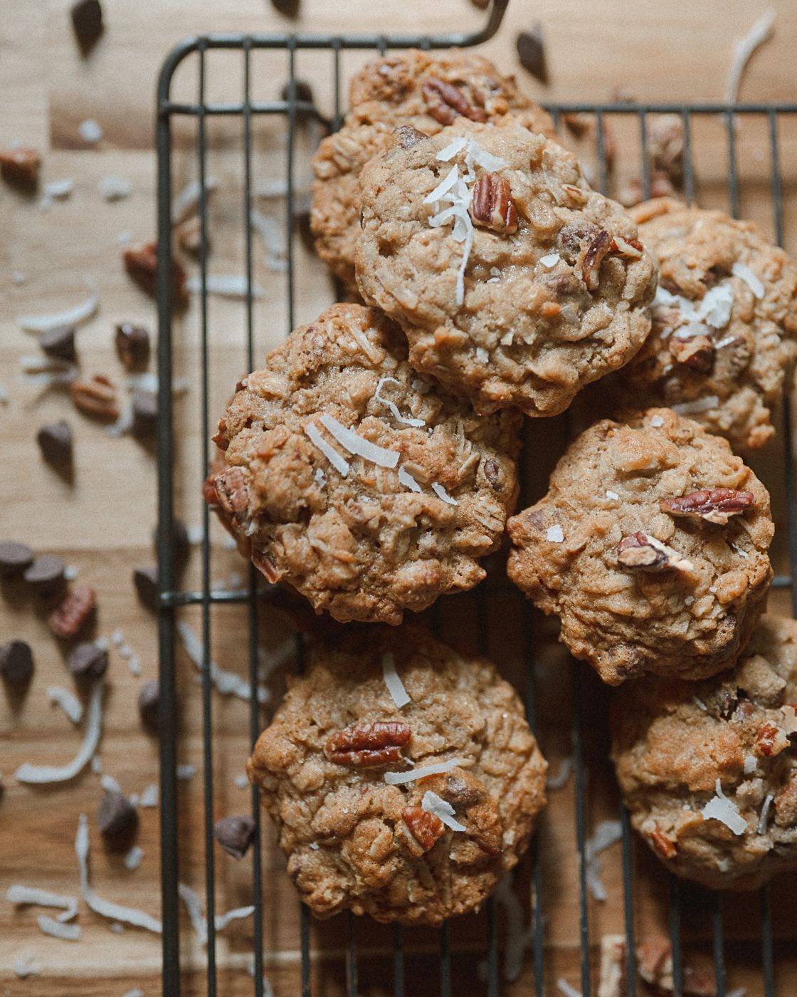 Homemade oatmeal pecan cookies with coconut flakes cooling on a wire rack against a wooden background.