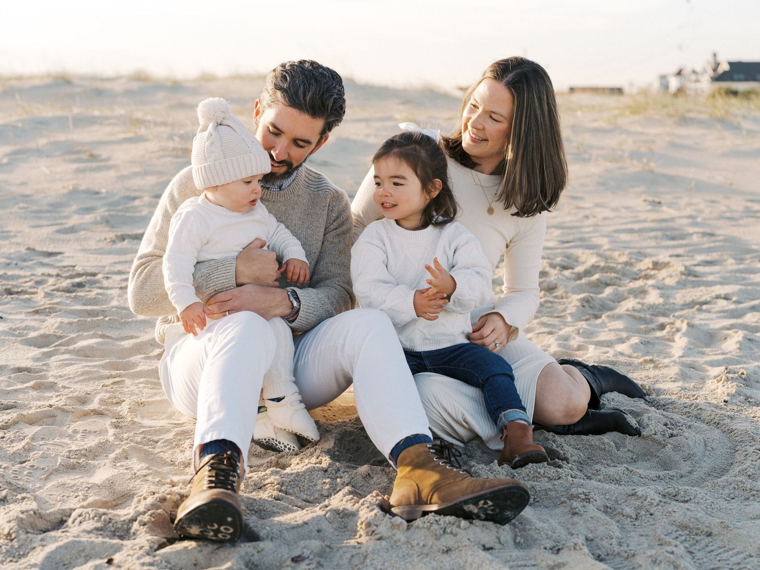Parents snuggling with their children on a quiet Monmouth County beach in autumn with cozy sweaters.