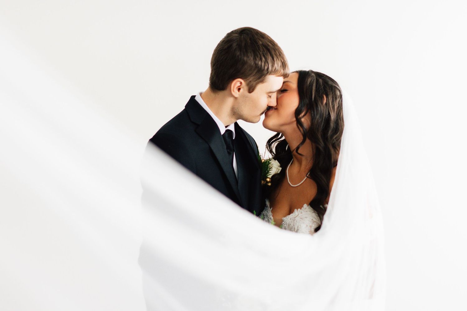 A romantic wedding photo of a couple kissing against a white background.