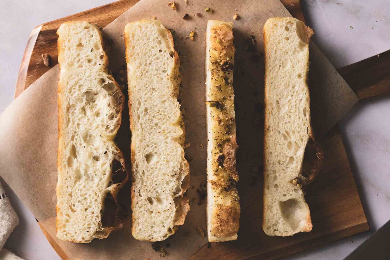 A golden-brown homemade bread loaf sliced and topped with herbs and seasonings on a wooden cutting board.