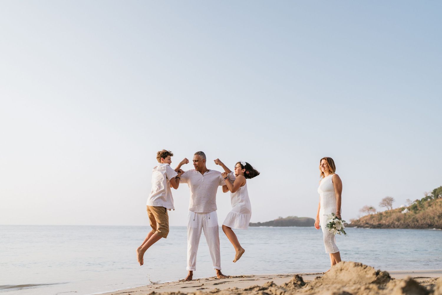 Family walking together on sandy beach with ocean waves in the background.