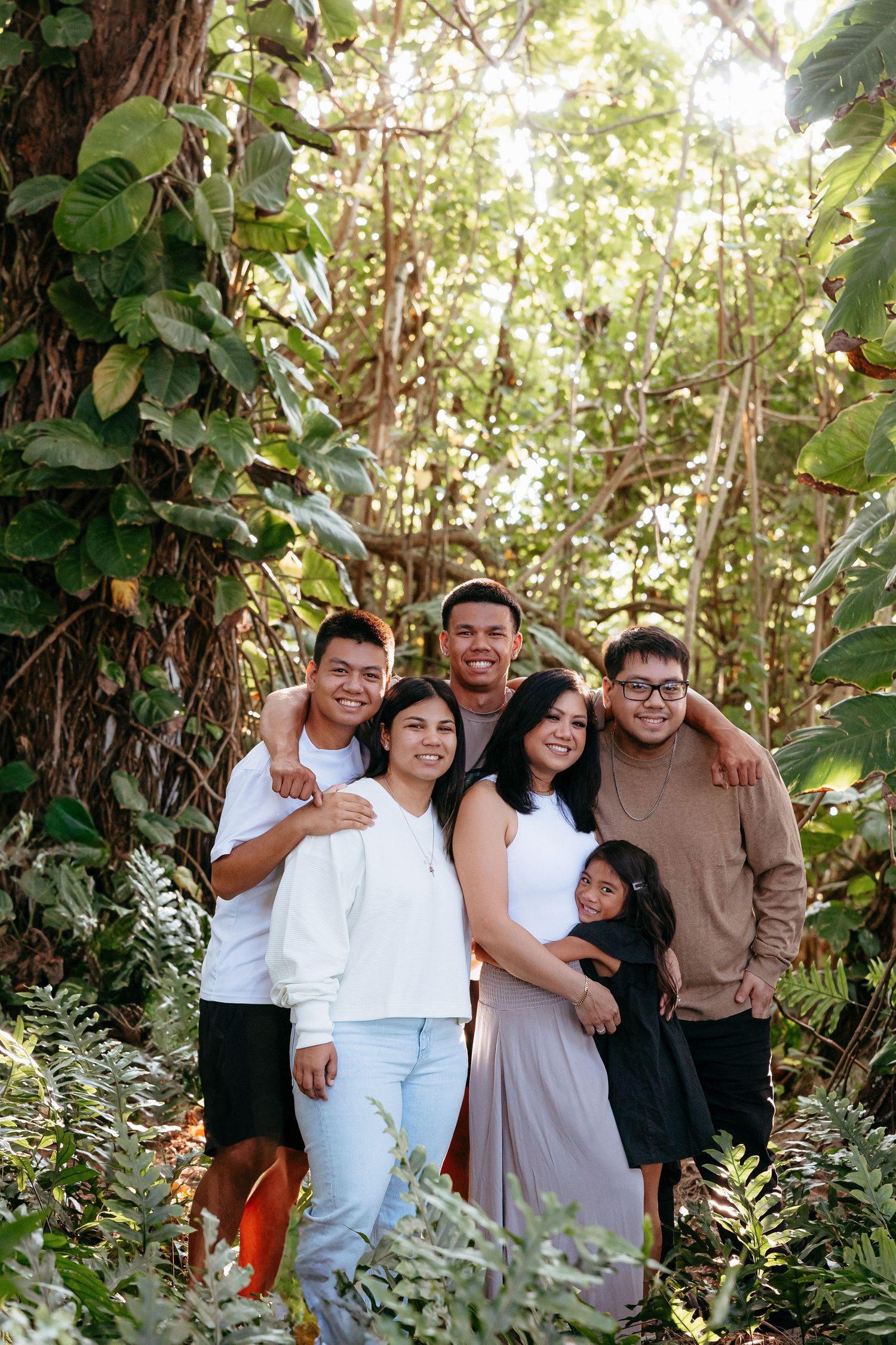 A group of people pose together outdoors in a lush garden setting with green foliage in the background.