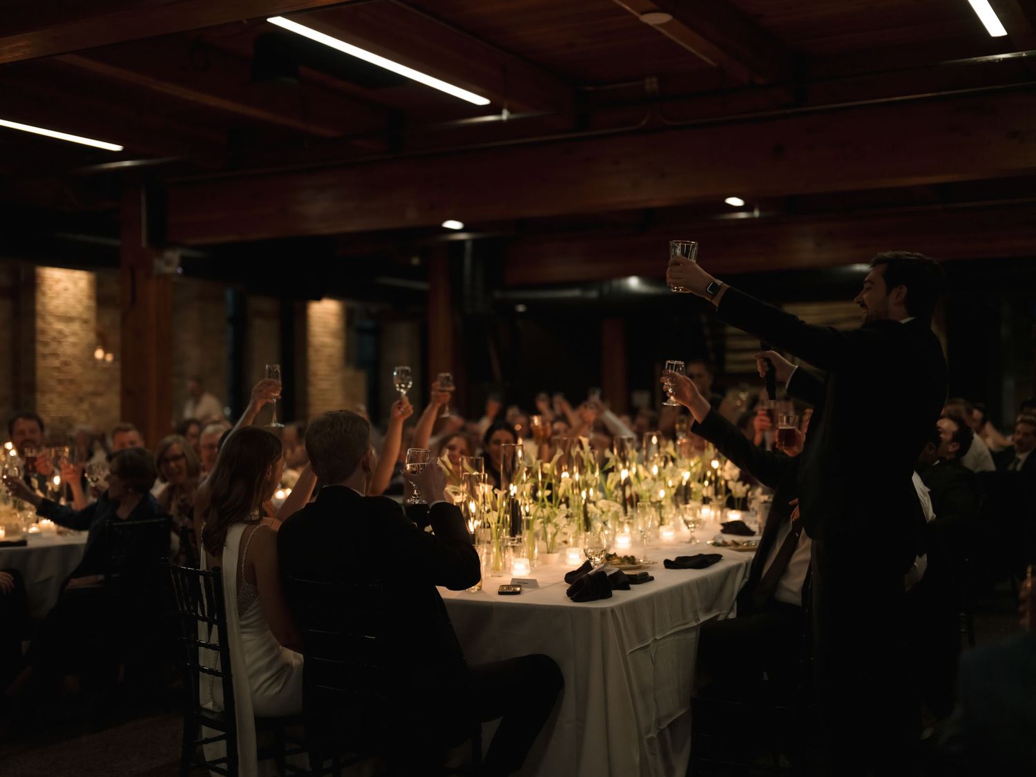 A dimly lit wedding reception venue with guests seated at tables and decorative lighting creating an intimate atmosphere.