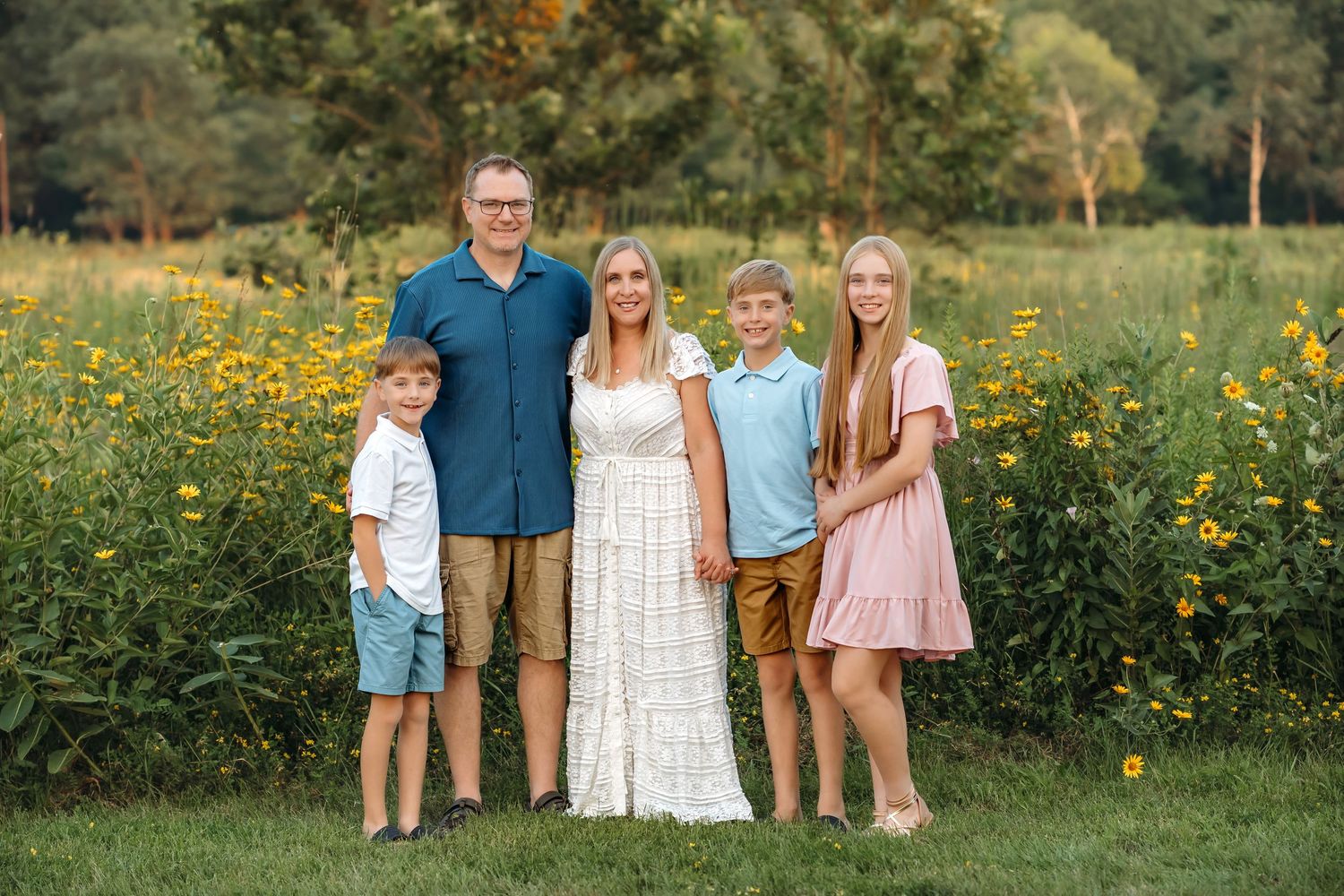 Family poses together in a wildflower meadow during sunset wearing coordinated blue and pink outfits.