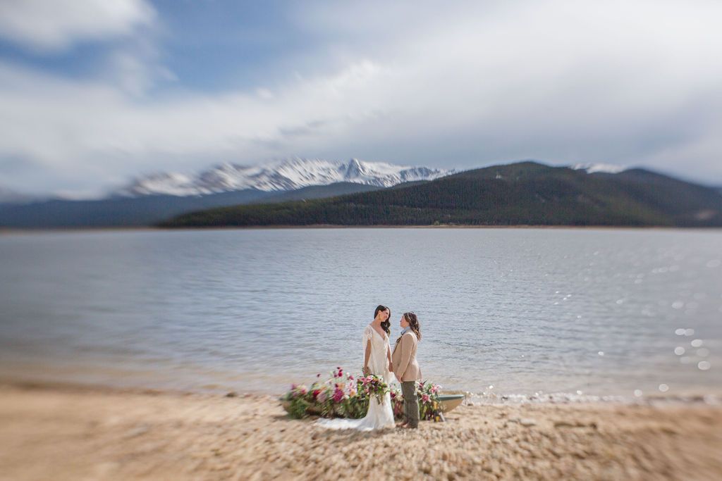 A mountain lake view with a pebble beach along the shore and snow-capped peaks in the distance.