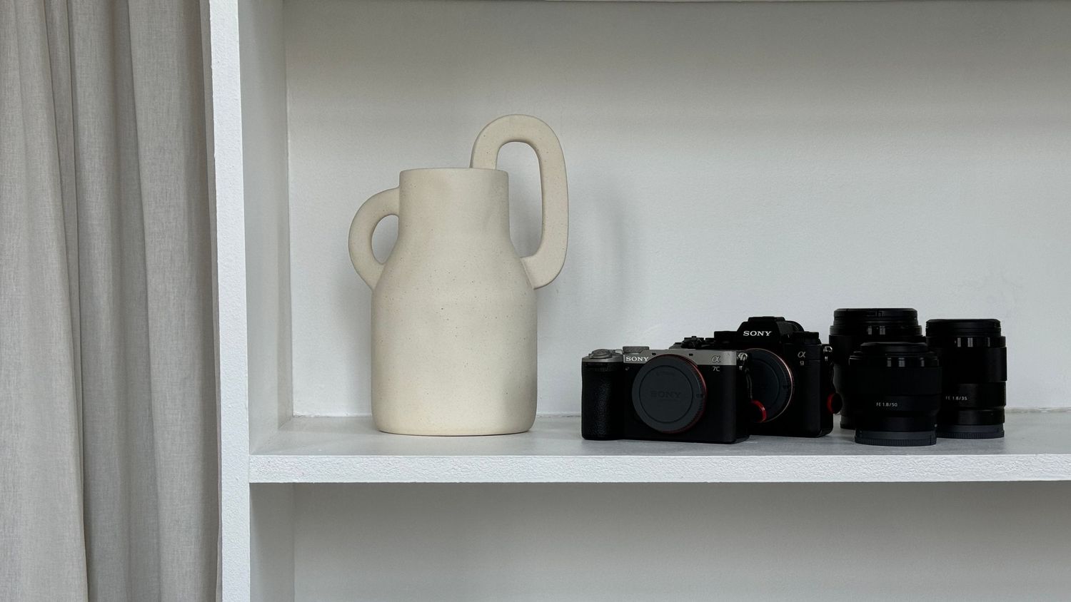 A photographer with long brown hair smiles while holding a professional camera in a casual indoor setting.