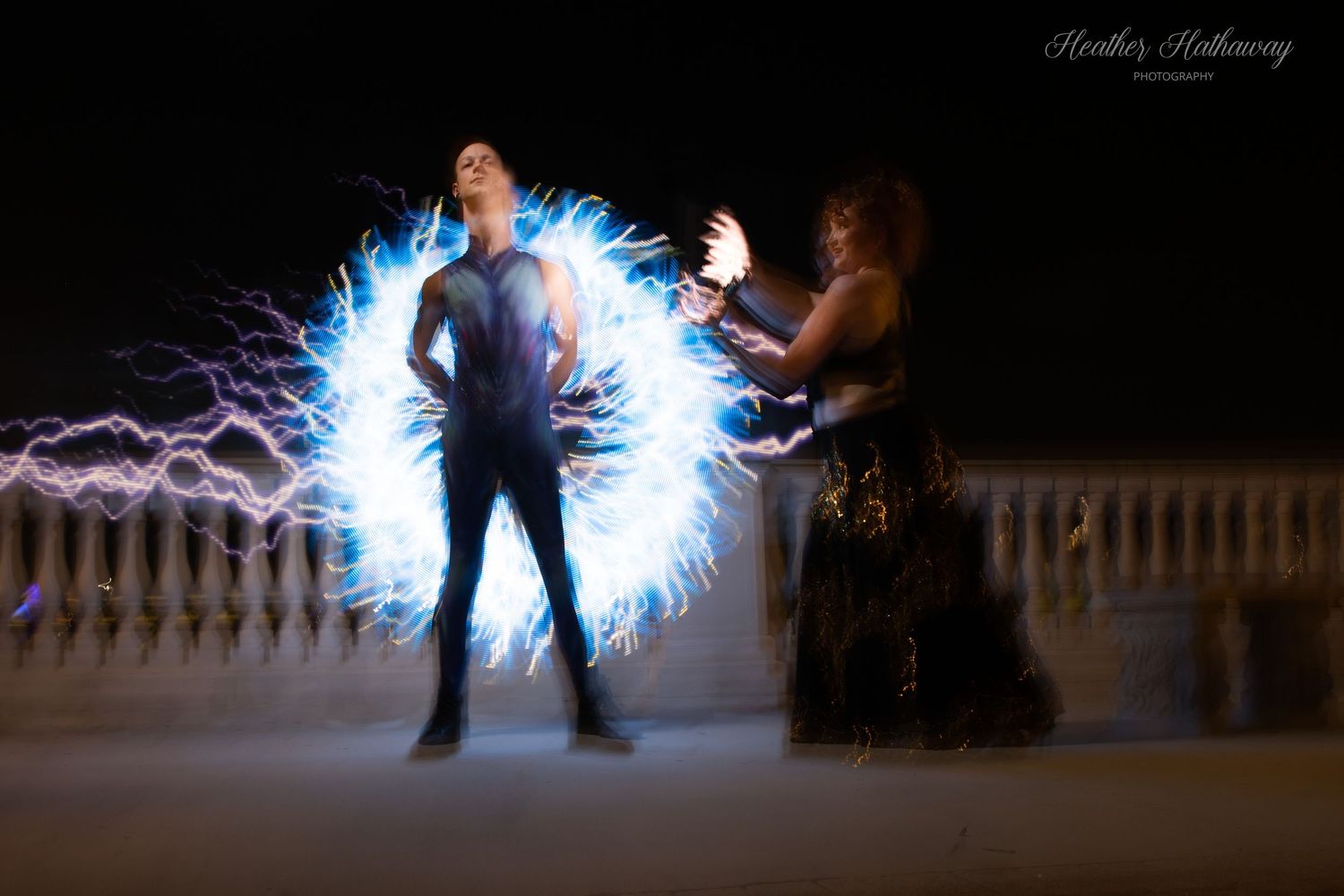 Long exposure light painting photography shows glowing blue circular pattern with silhouettes against dark background.