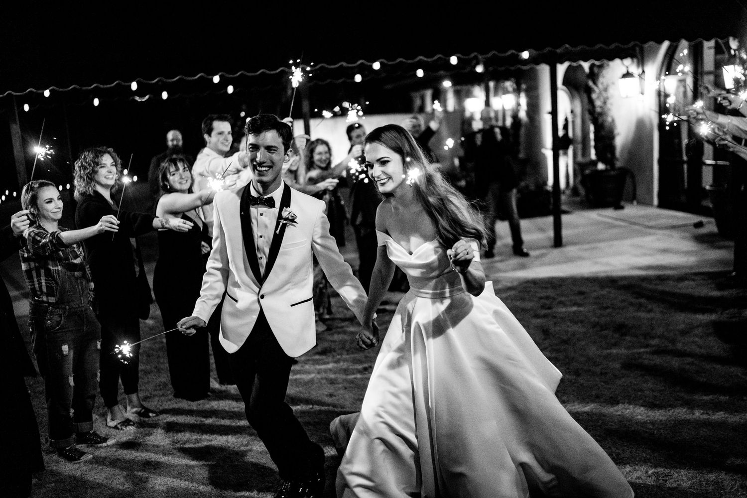 Reception DJ plays music on professional equipment while entertaining dancing wedding guests on a dark dance floor.