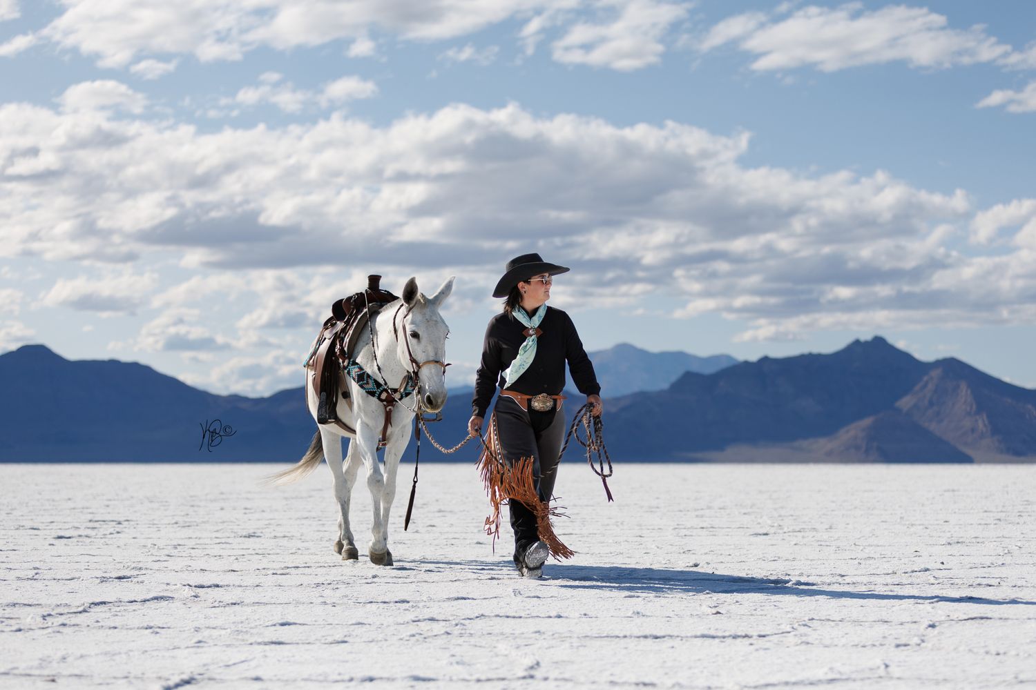 Horses and riders traverse across a snowy landscape with mountains in the background.