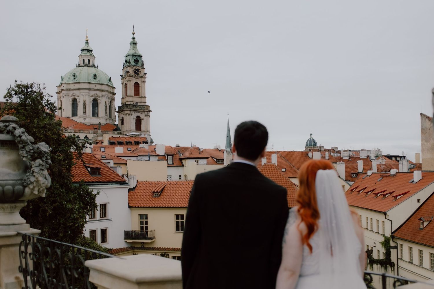 Romantic wedding scene with couple dancing by Charles Bridge in Prague along the Vltava River on a cloudy day.