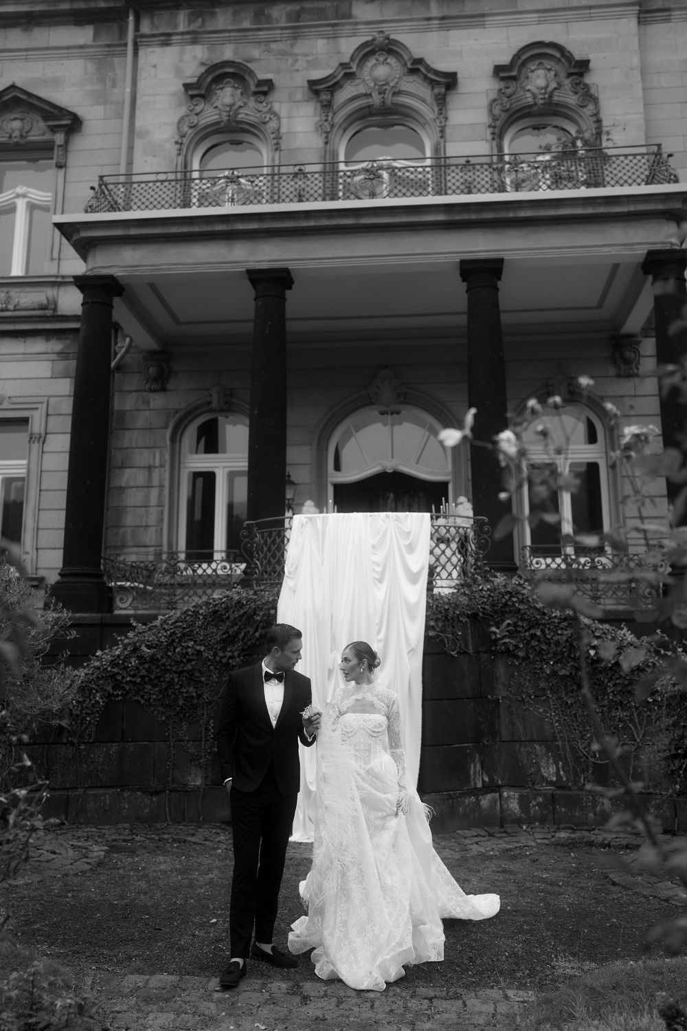 A black and white photo series showing flowing white fabric or material draped across a lawn in front of buildings.