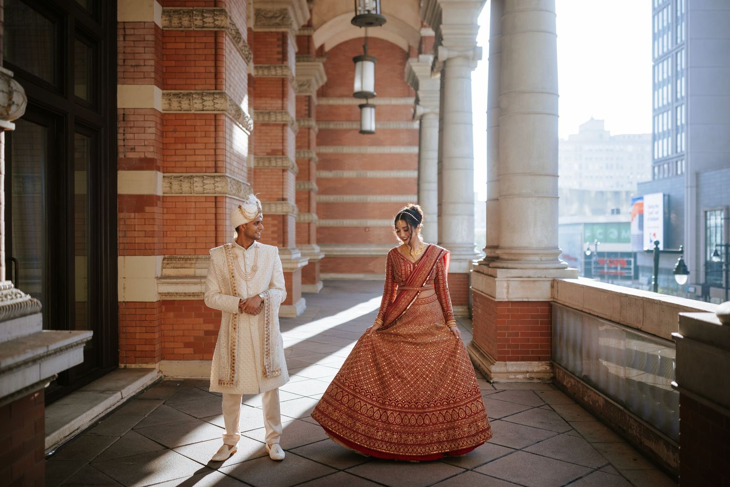 A couple poses for wedding photos in an elegant brick archway corridor with dramatic lighting and architectural details.