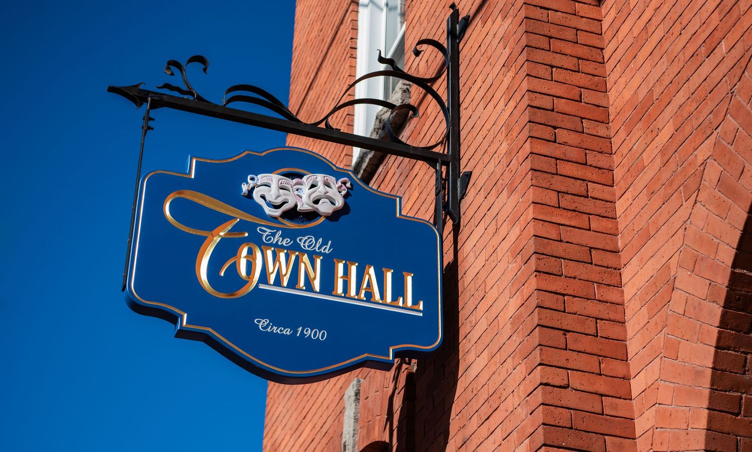 A decorative blue and gold Town Hall sign mounted on a red brick building against a vivid blue sky.