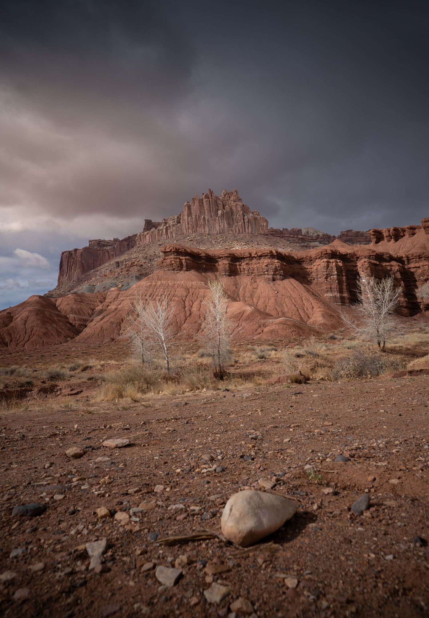 Dramatic storm clouds loom over red rock formations at Capitol Reef National Park with barren desert landscape in foreground.
