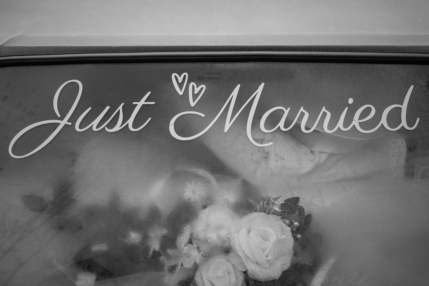 Black and white photo of 'Just Married' text with heart design and roses visible through frosted glass surface.