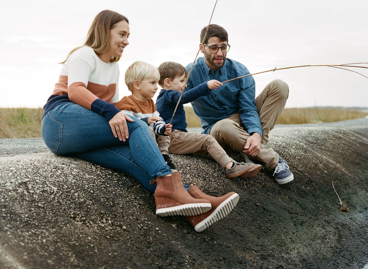 Family sitting together on rocks enjoying a fishing activity.
