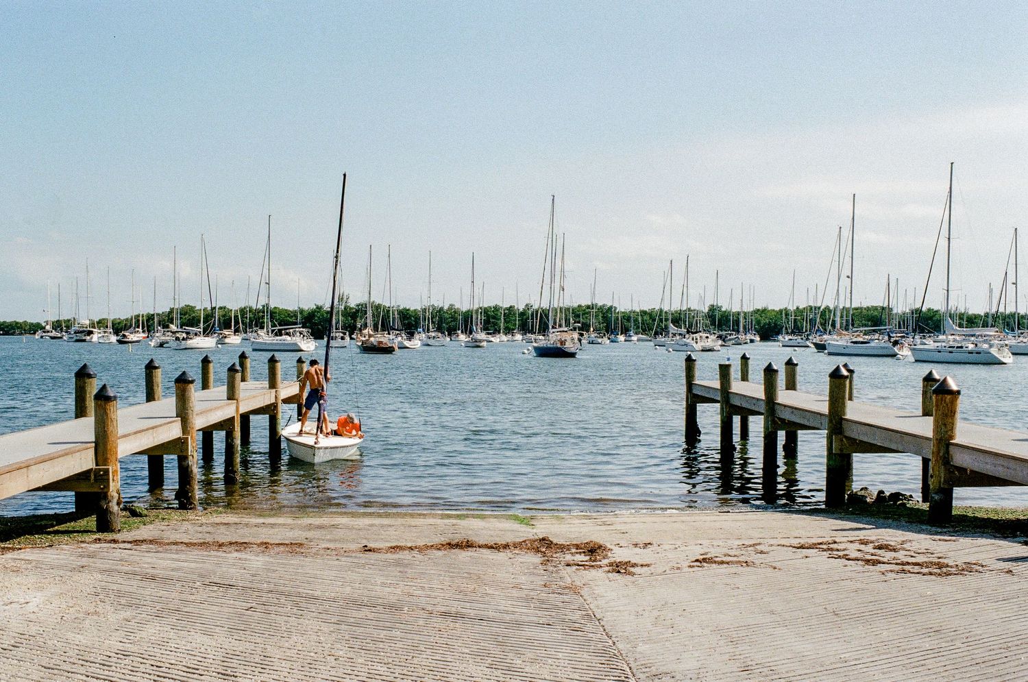 Sailboats anchored between two wooden docks at a marina with calm blue waters and clear skies.