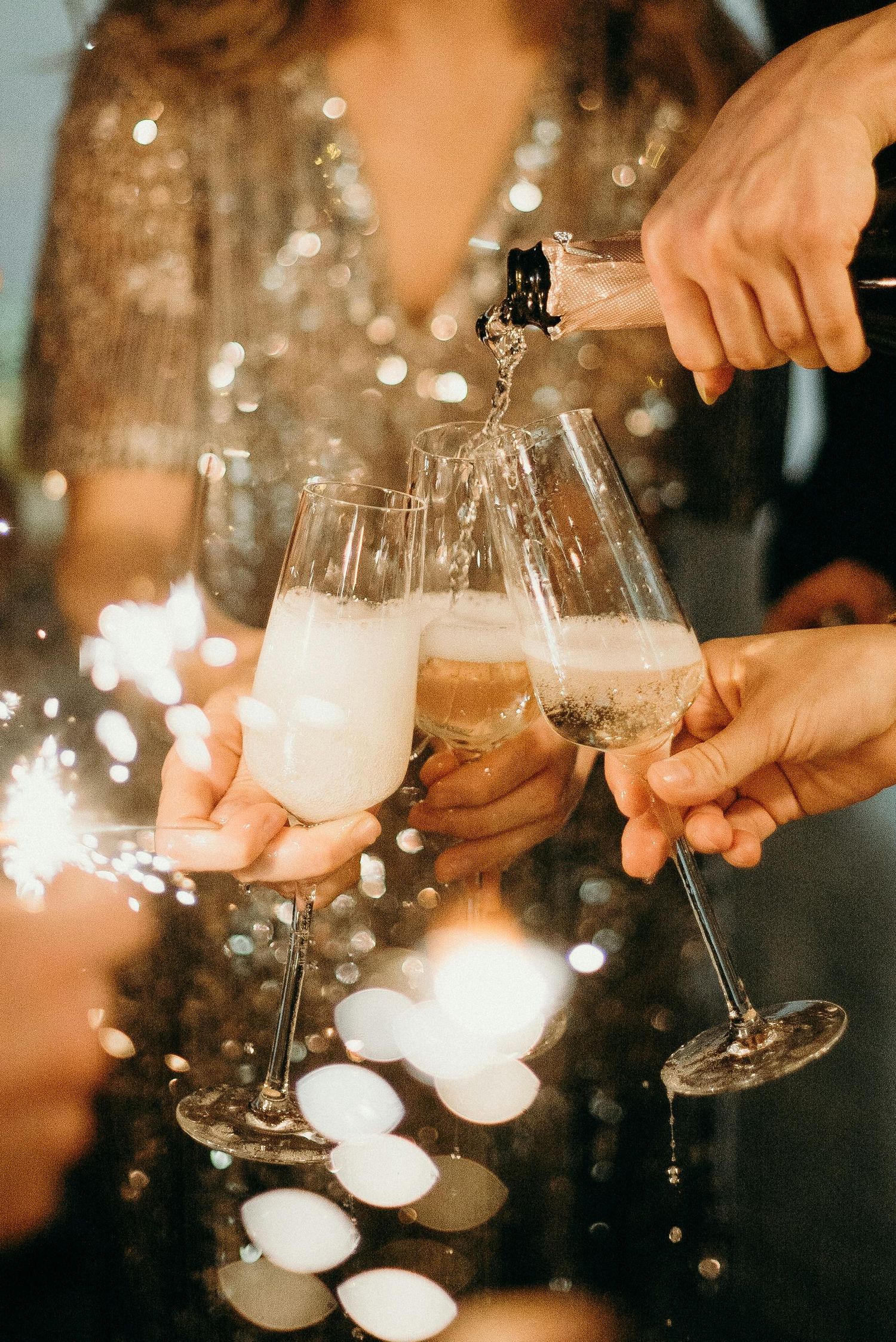 Hands pouring and toasting with champagne glasses against sparkling bokeh lights creating a festive celebration bachelorette party pa.