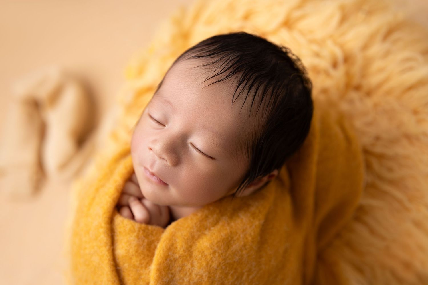 Peaceful sleeping newborn wrapped in soft yellow blanket during professional photo session.