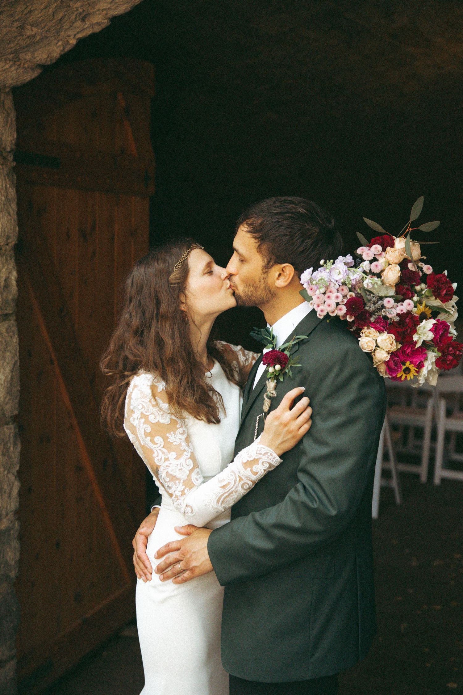 A romantic kiss captured between newlyweds with a colorful floral bouquet.