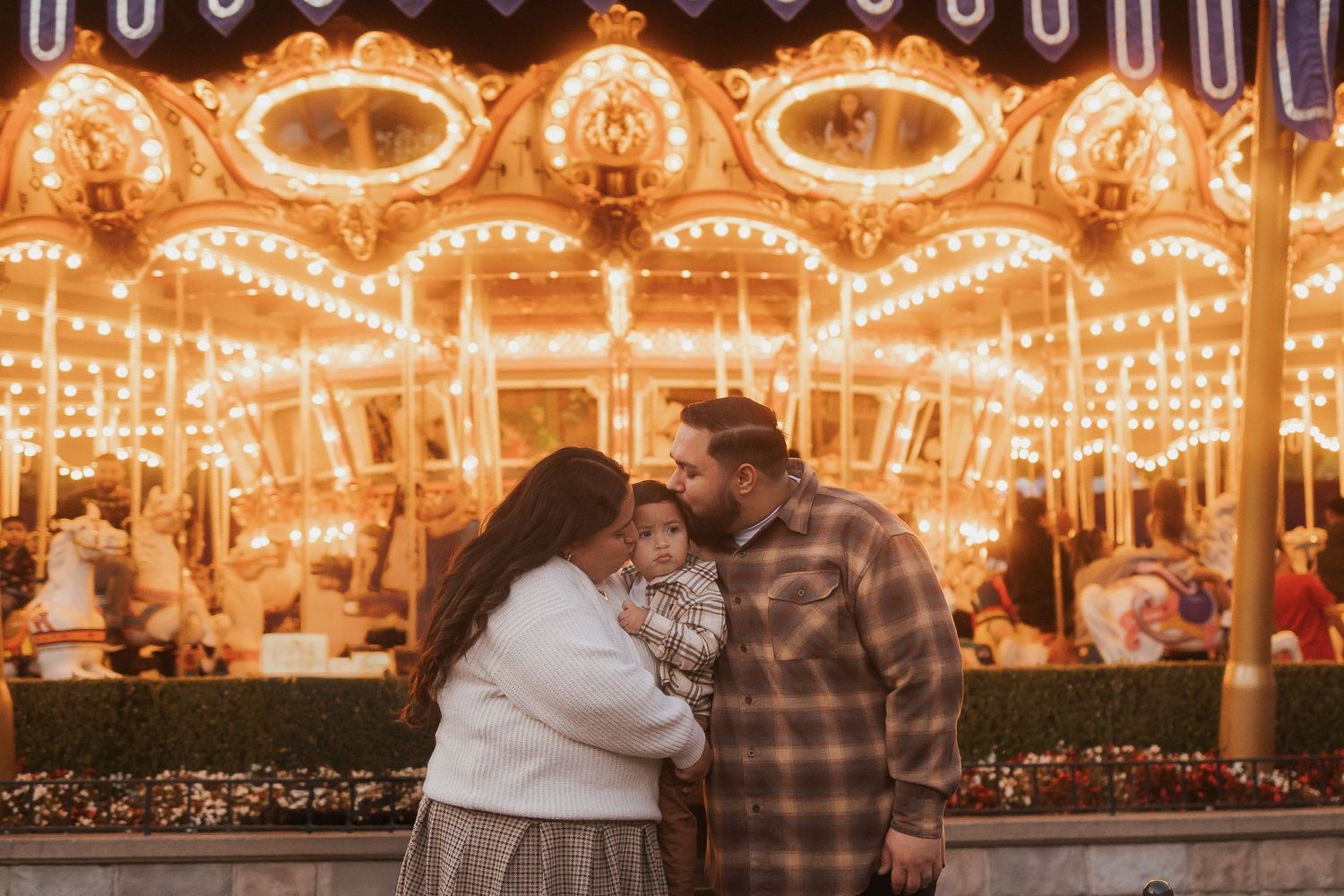 Couple embraces in front of illuminated carousel at night.