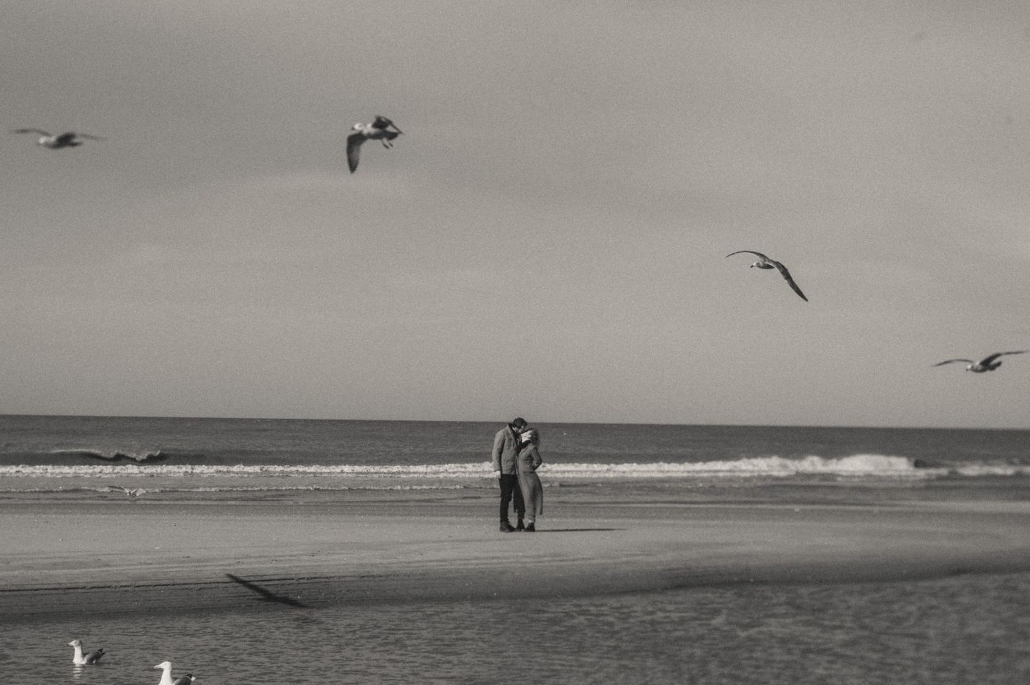 An intimate black-and-white shot of the couple embracing with the ocean behind them.