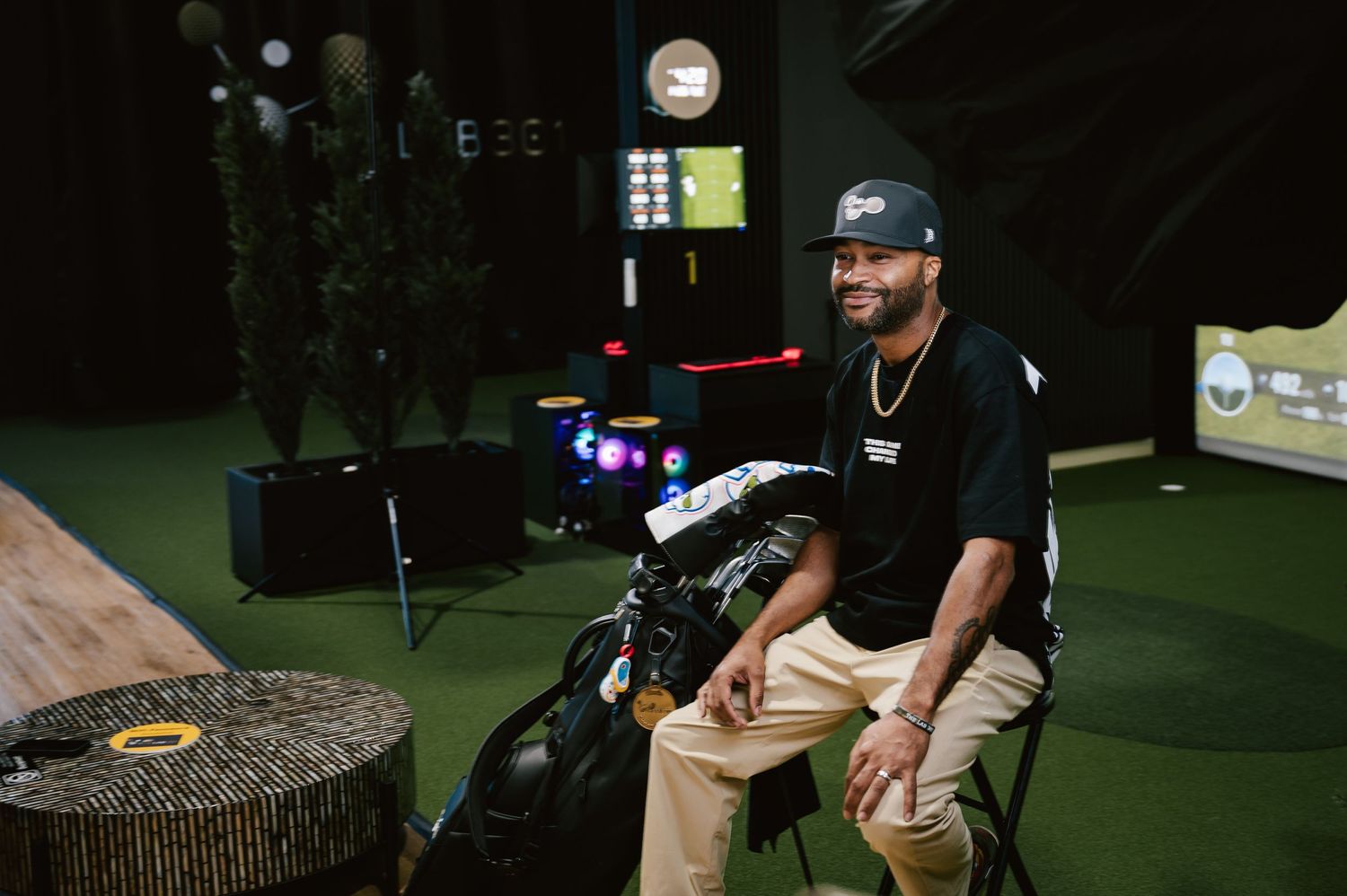 Person in casual attire sits on equipment in an indoor sports facility with green turf.
