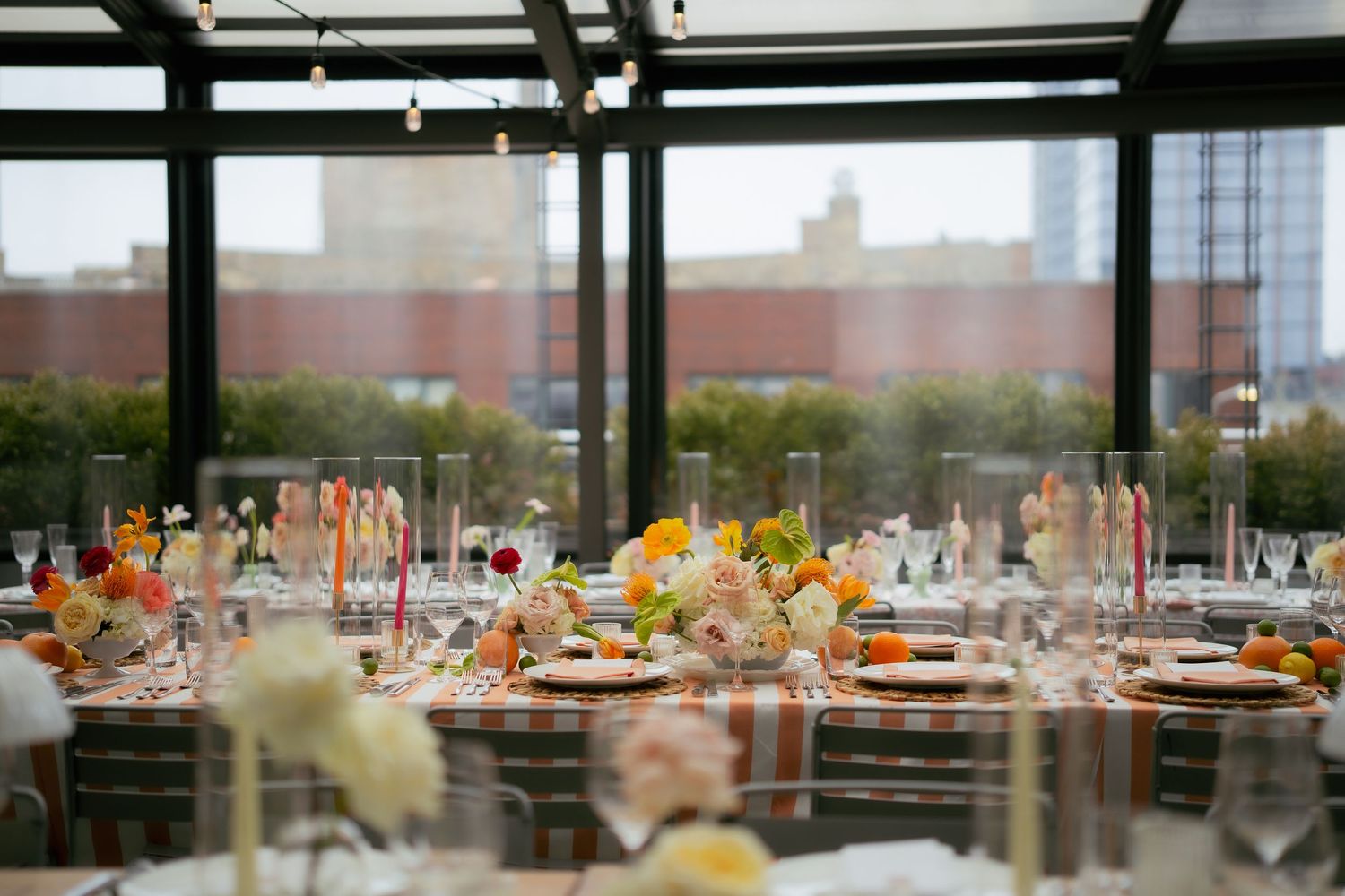 Elegant wedding reception table with orange and white floral centerpieces in modern venue with city views.