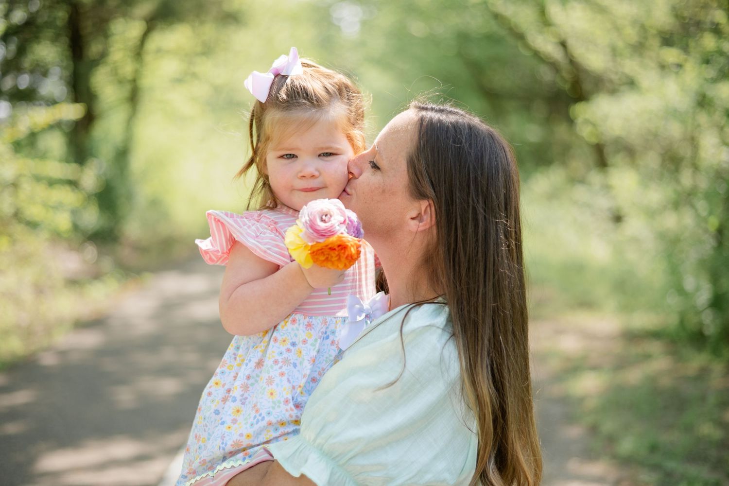 A loving parent and child share a joyful moment on a wooded path while holding a pink bubble wand.