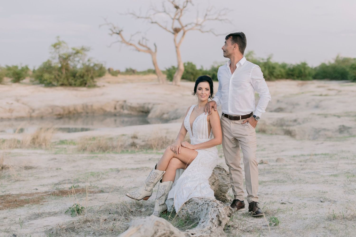 Couple posing in arid African landscape with baobab trees during golden sunset.