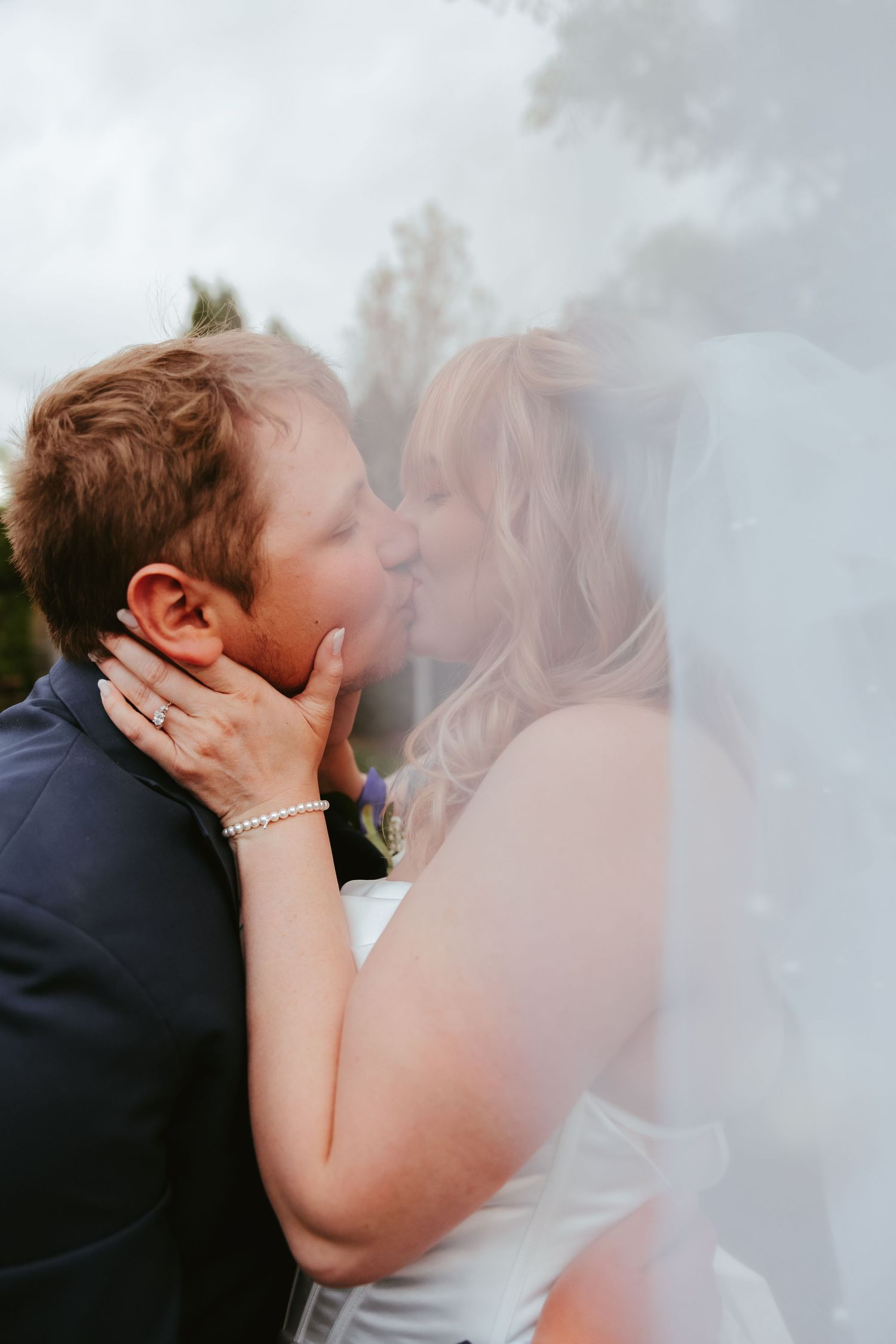 A romantic wedding moment shared between a couple as they embrace and kiss under a misty sky.
