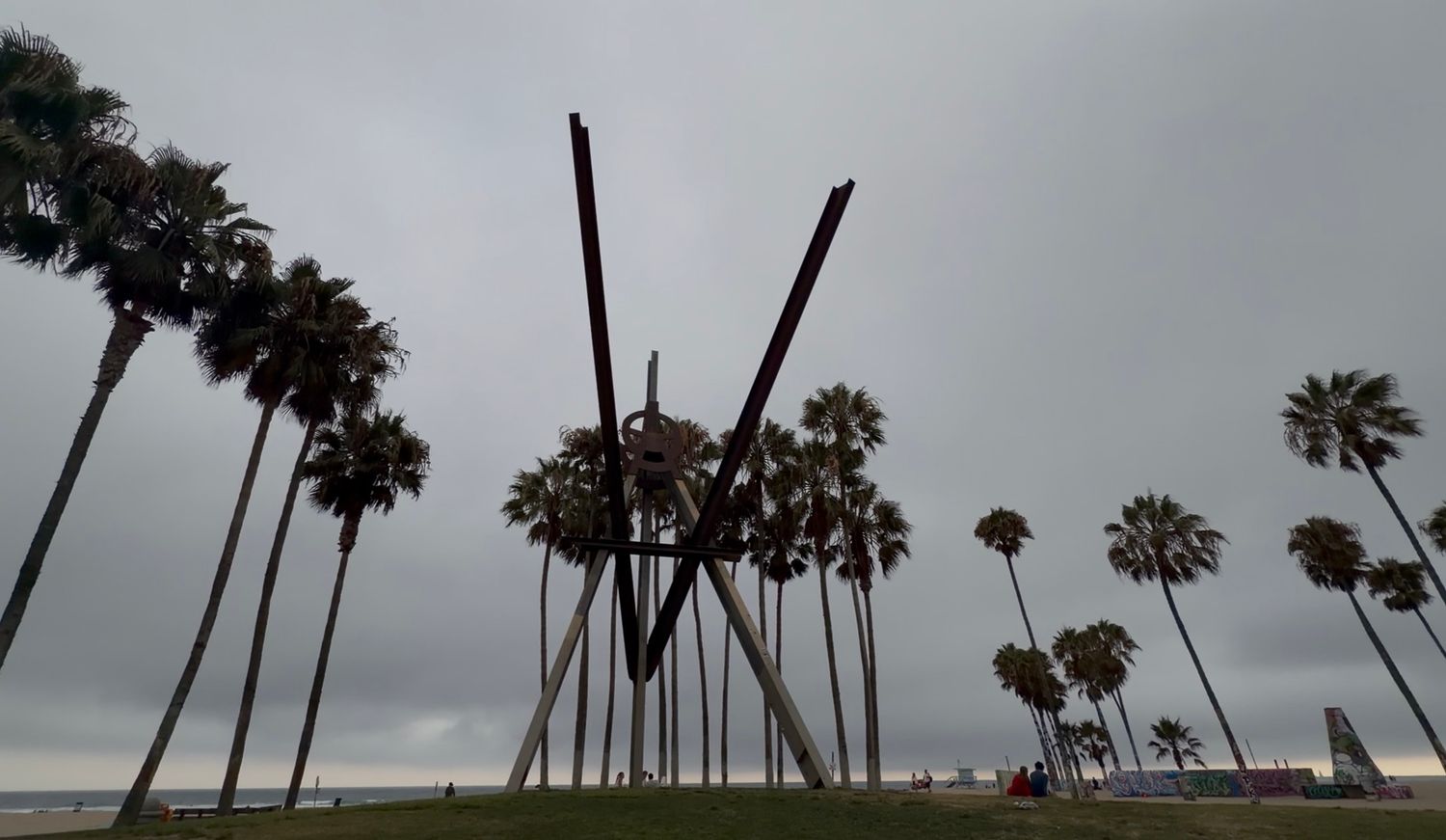 Abstract metal sculpture rising among palm trees on overcast Venice Beach, Los Angeles, California.