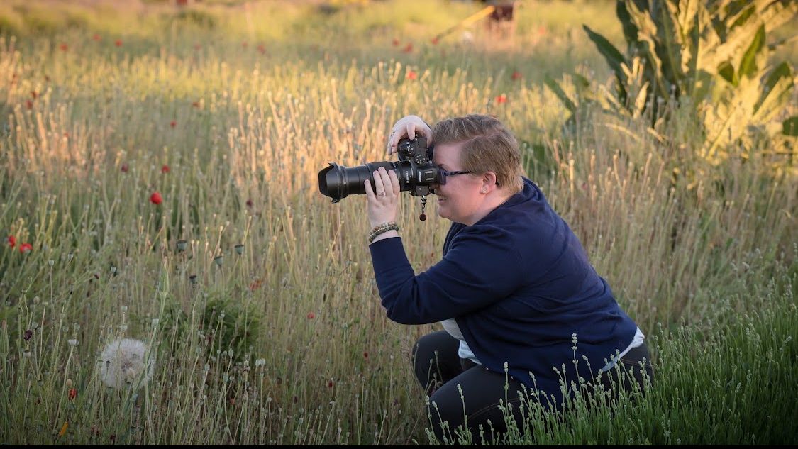 Photographer Deidra Dixie crouching in a wildflower meadow capturing images with a telephoto lens during golden hour.