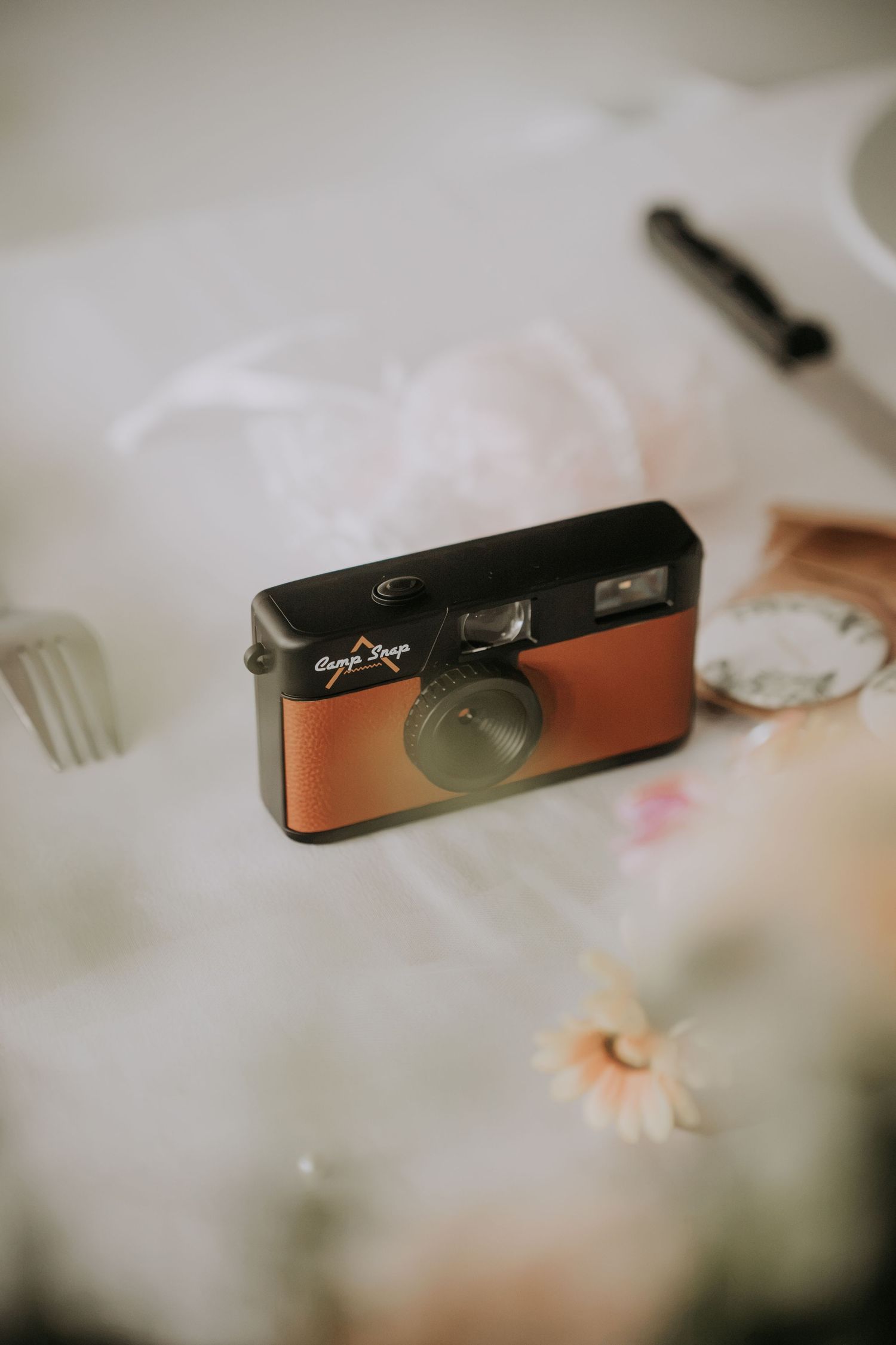 Vintage retro film camera with brown leather detail placed on a white table with flowers and cutlery.