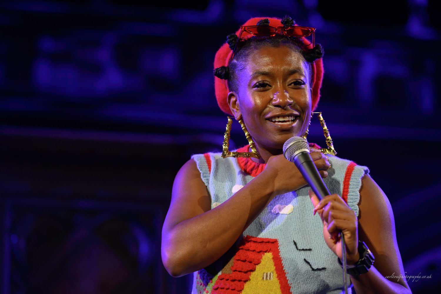 A performer in a yellow dress sings passionately on stage under dramatic blue and red lighting.
