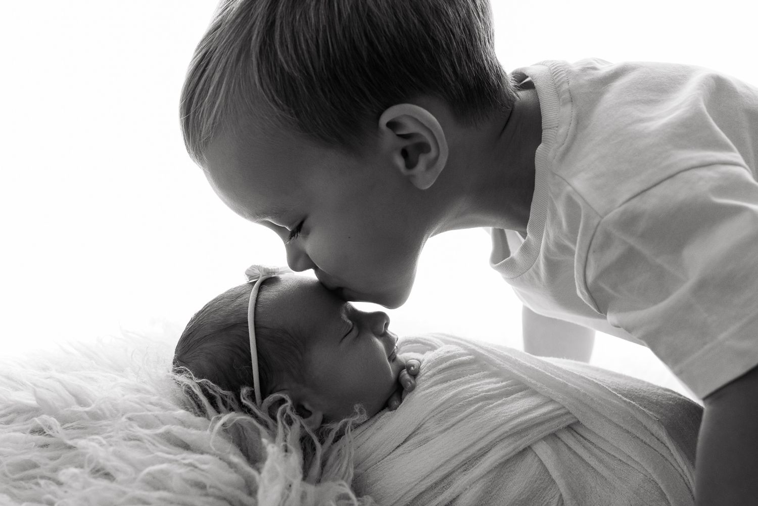 Black and white newborn photo of a brother cradling his sleeping baby sister, captured by Little Wonders Photography.