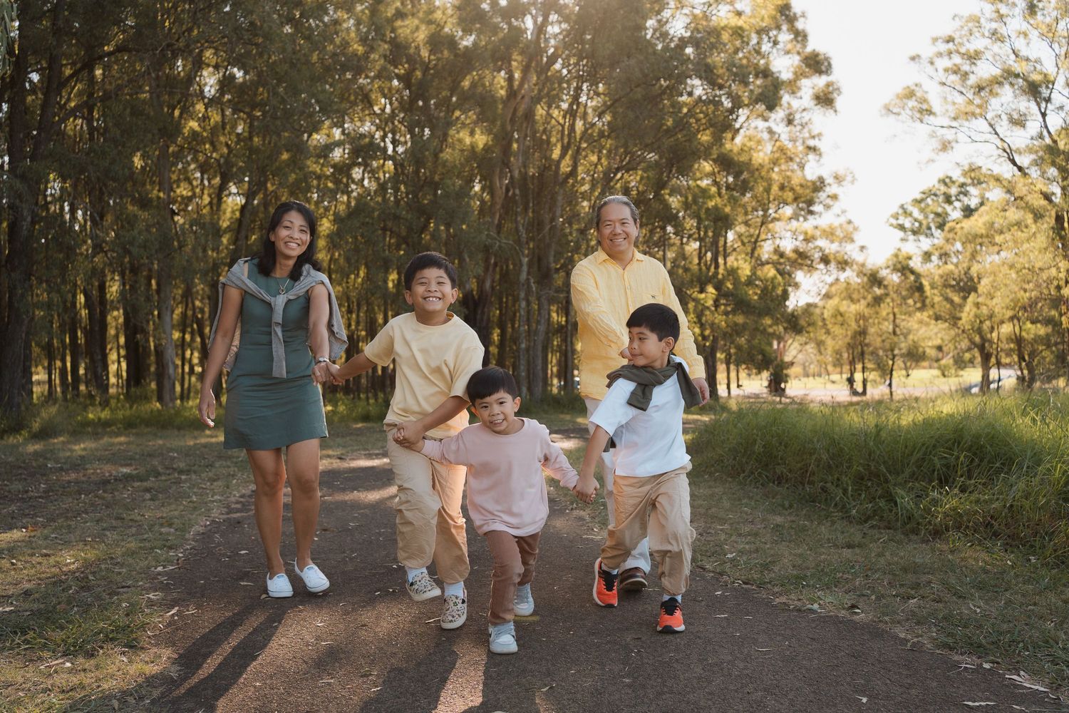 family of five walking together on a forest path, smiling and holding hands on a sunny day during a photoshoot in sydney rouse hill