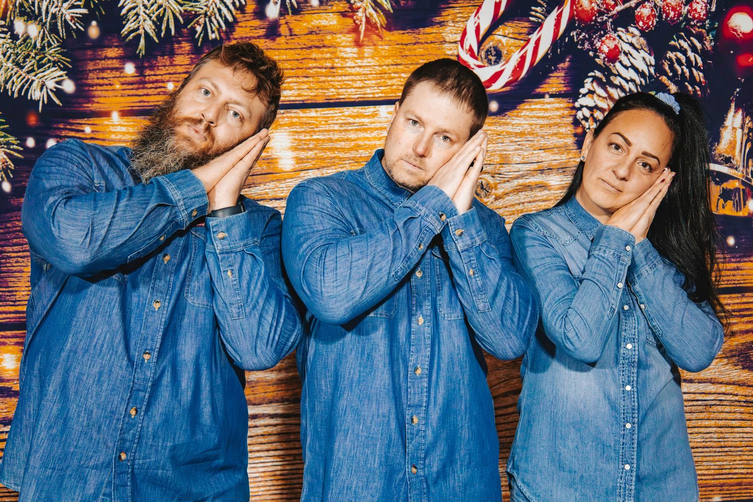 Three people in matching denim shirts pose together making see no evil, hear no evil, speak no evil gestures.