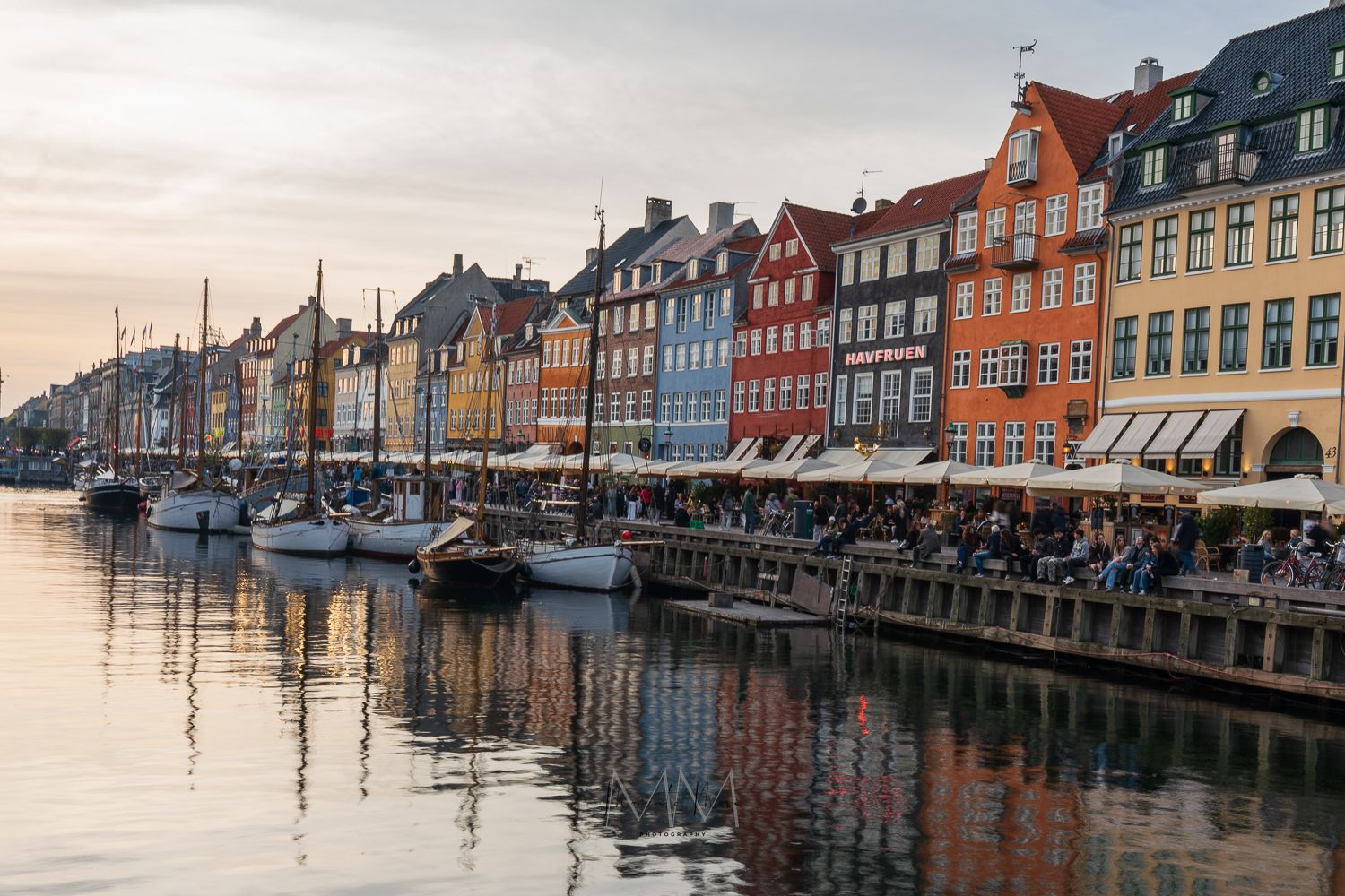 Nyhavn canal waterfront at sunset with colorful historic buildings and sailing boats.