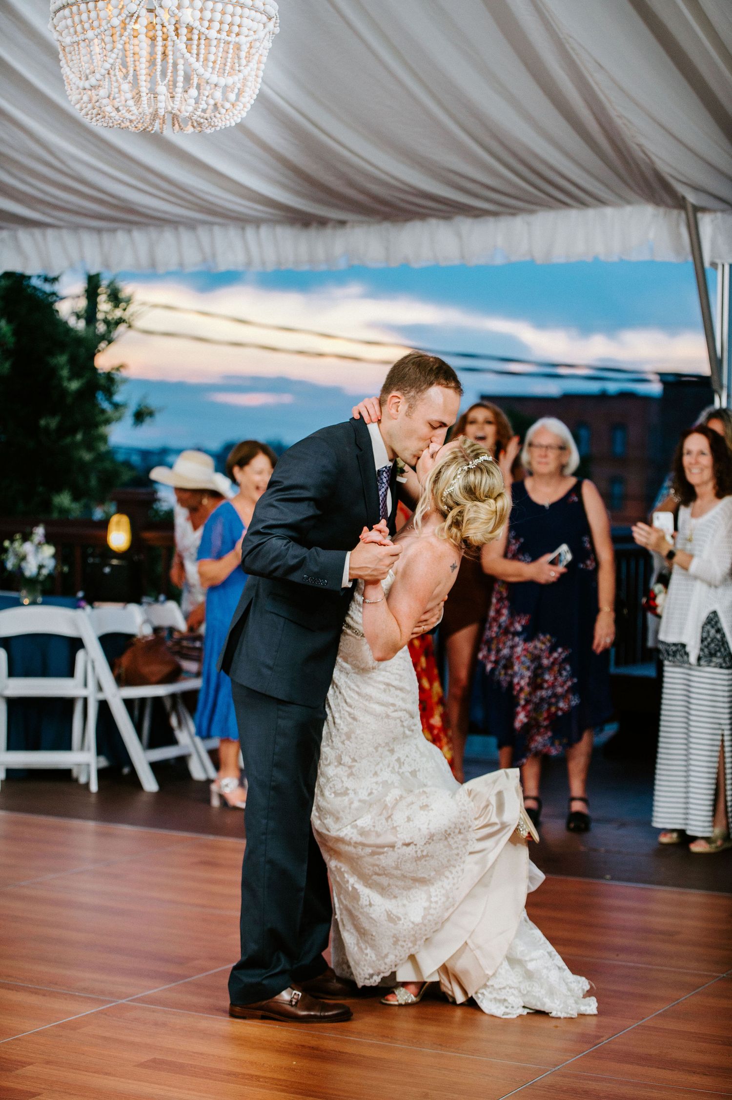 A couple performs a romantic dance dip on a wooden dance floor under an elegant white tent at their wedding reception.