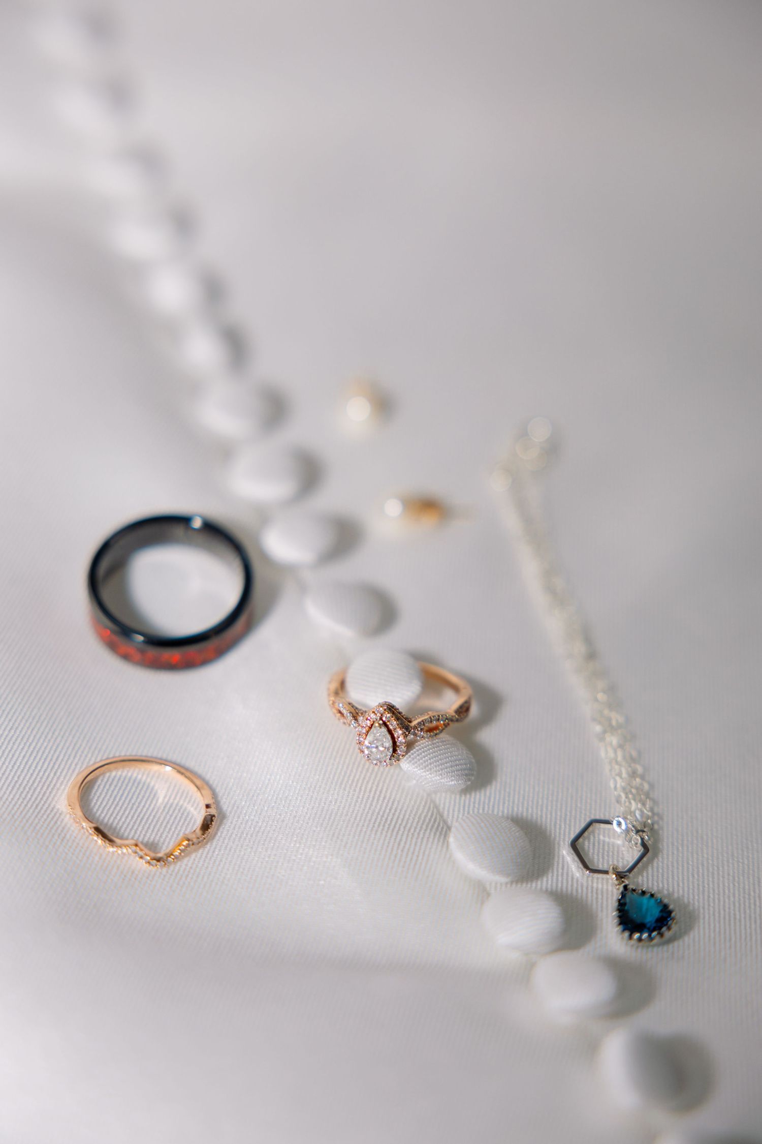 Delicate rose gold engagement rings and jewelry pieces arranged artistically on a soft white textured surface.